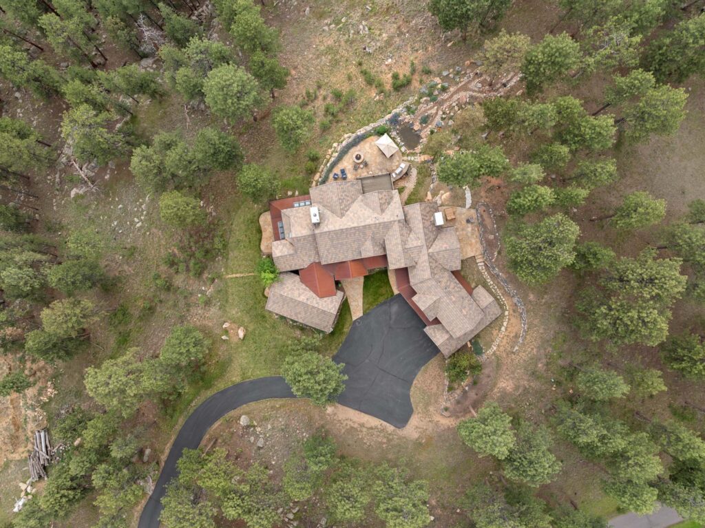 Top-down aerial drone photography of a chalet-style mansion in Evergreen, Colorado highlighting the driveway, surrounding land, and trees
